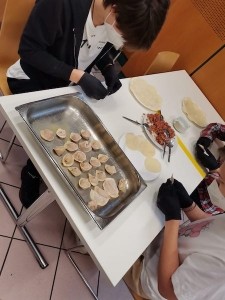 Two boys with black gloves sitting at a table making dumplings